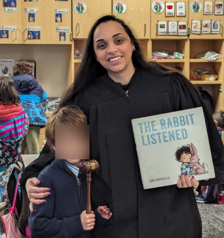 Judge Rampersad poses with a student and reading book in class.